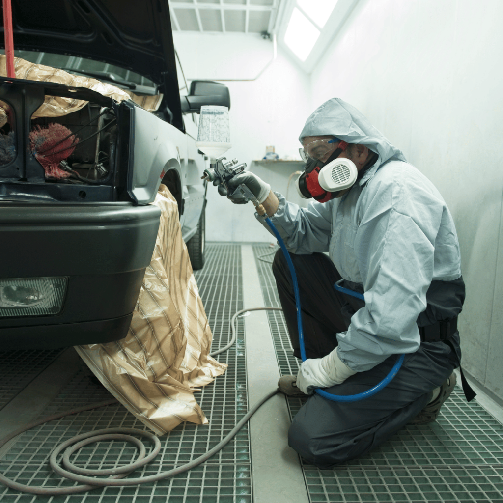 Technician painting a car in a spray booth at a certified auto body shop using professional equipment